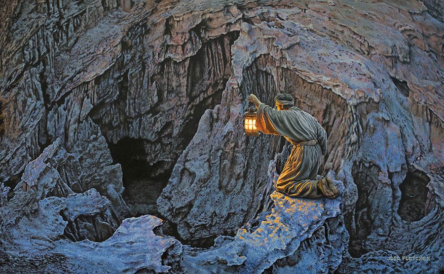 A man wearing a robe holds a lantern toward a mysterious cave.